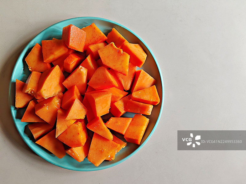 白色背景上，蓝绿色陶瓷盘中放着新鲜切片、成熟的木瓜水果，静物写生图片素材