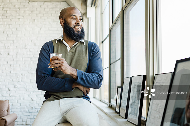 Smiling man by window with drink图片素材