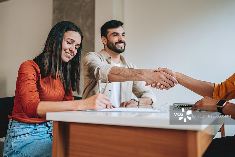 房地产经纪人与客户握手，其妻子正在签署合同图片素材