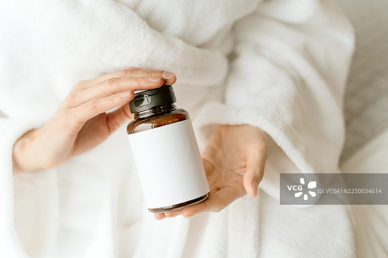 身着白色长袍，手持贴有空白标签的棕色玻璃瓶，象征健康或保健品概念图片素材