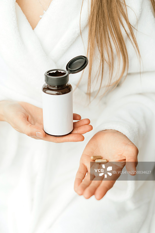 身穿白色长袍的人手中拿着一瓶含有胶囊的补充剂图片素材