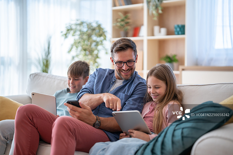 父亲和孩子们在沙发上愉快地使用电子设备图片素材