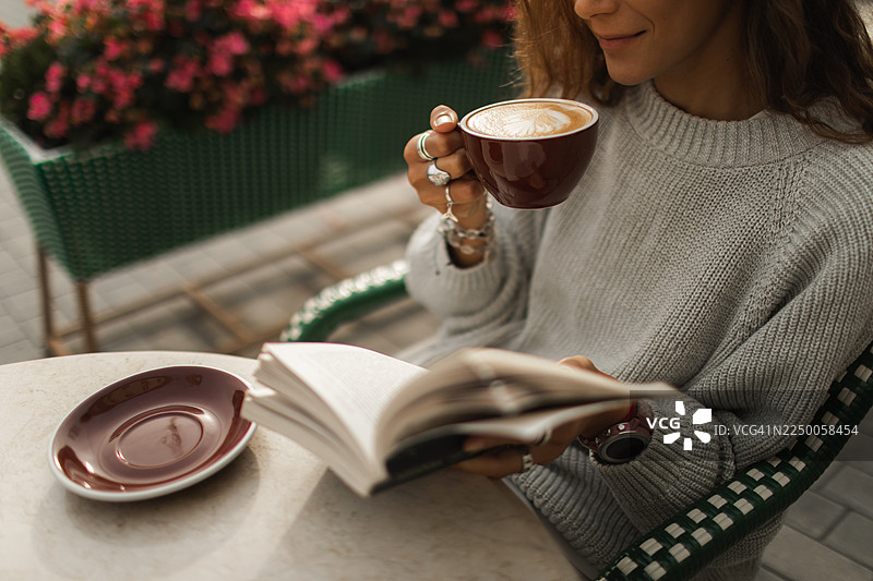 温馨咖啡时光：女子在户外边喝咖啡边读书图片素材