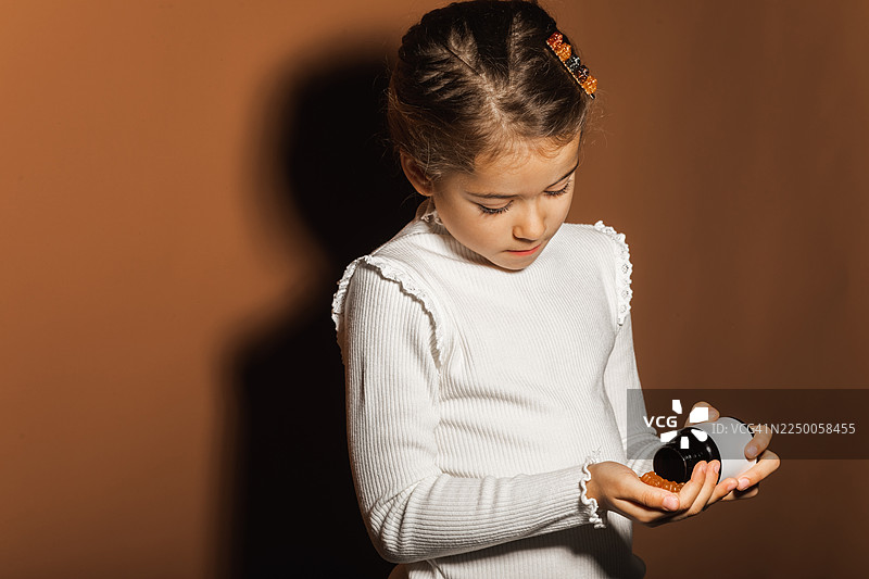 穿着白色针织毛衣的小女孩，手里拿着一个面霜罐，低头看着护肤品罐子图片素材