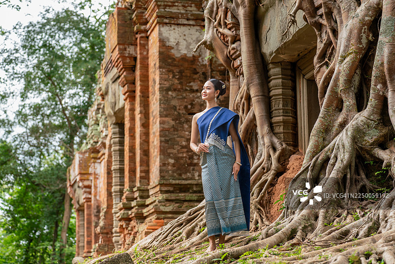 身着柬埔寨传统高棉服饰的柬埔寨女性在暹粒吴哥窟的科克寺普拉姆神庙前摆拍。亚洲女性在古代寺庙遗址前留影。图片素材