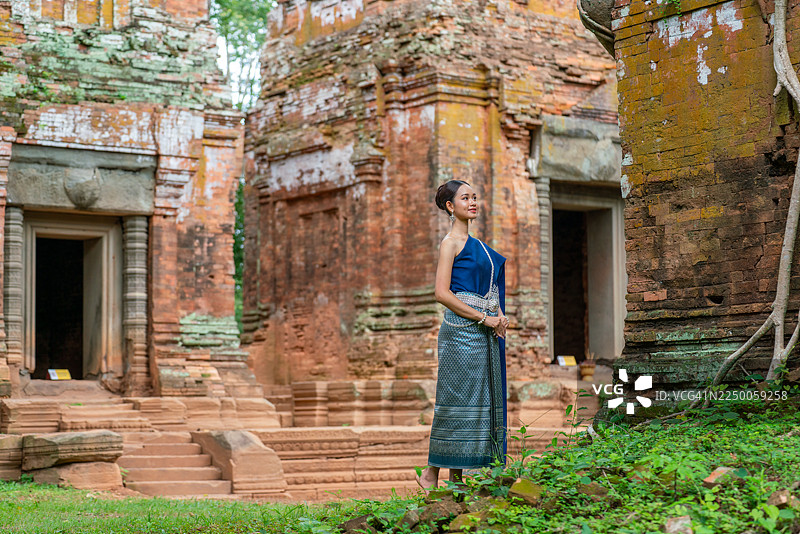 柬埔寨女人身着传统高棉服装，在暹粒吴哥窟戈公寺的普拉萨普拉姆古庙遗址前摆姿势。亚洲女性在古庙遗址前拍照。图片素材