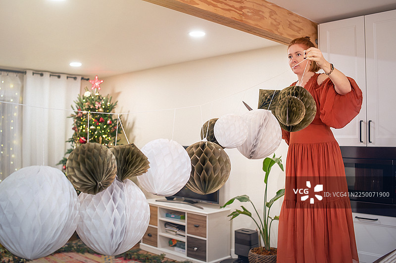 在新泽西州现代住宅中悬挂节日纸装饰品，为节日庆典做准备。一位女士正在为冬季节日做准备。图片素材