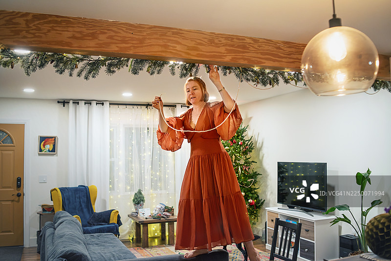 37岁的女性在新泽西州精心布置节日家居装饰，将花环和灯饰挂在天花板的横梁上。图片素材