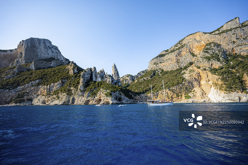 excursion boat off picturesque rocky coast, cliffs with caves in morning light, L'Aguglia rock pin, blue sea and Cala Goloritzé beach, Golfo di Orosei, Baunei, Sardinia, Italy图片素材