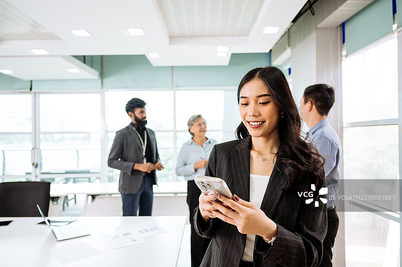 多元化的商务人士在现代办公室穿着得体的商务装协同工作，其中一位中国女商人正在使用智能手机图片素材