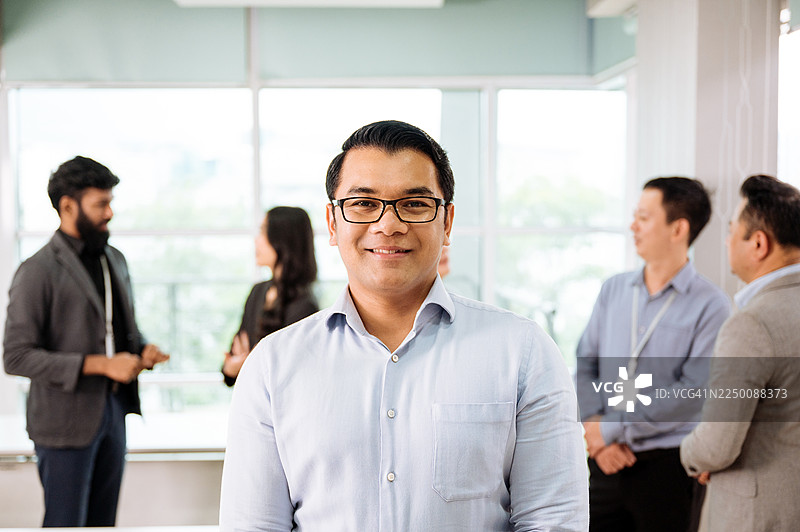 多元化的商务人士在现代办公室协作，身着得体的商务装，面带微笑看向镜头图片素材