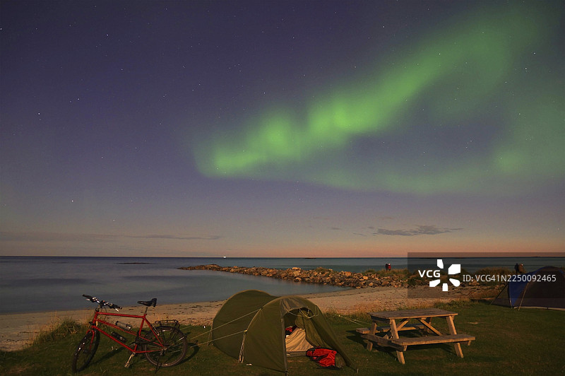 夜间，挪威诺尔兰郡韦斯特伦群岛兰尧亚岛布莱克的沙滩上空，绿色的北极光与星空，帐篷和自行车图片素材