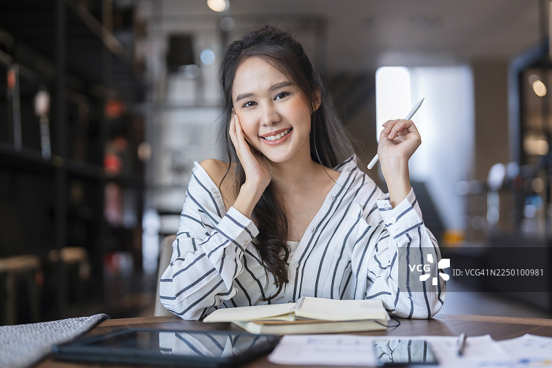 一位穿着商务休闲装的亚洲女企业家，在现代办公室或当代仓库展厅内，在与客户进行在线会议的间隙放松休息，展现出专业和时尚感。图片素材