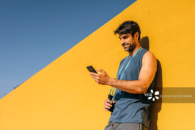 一名年轻男子倚靠在墙边，使用智能手机的肖像照图片素材