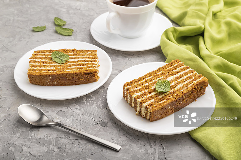自制蜂蜜蛋糕搭配奶油和薄荷，旁边放着一杯咖啡，置于灰色混凝土背景和绿色织物上。侧面视角，特写。图片素材
