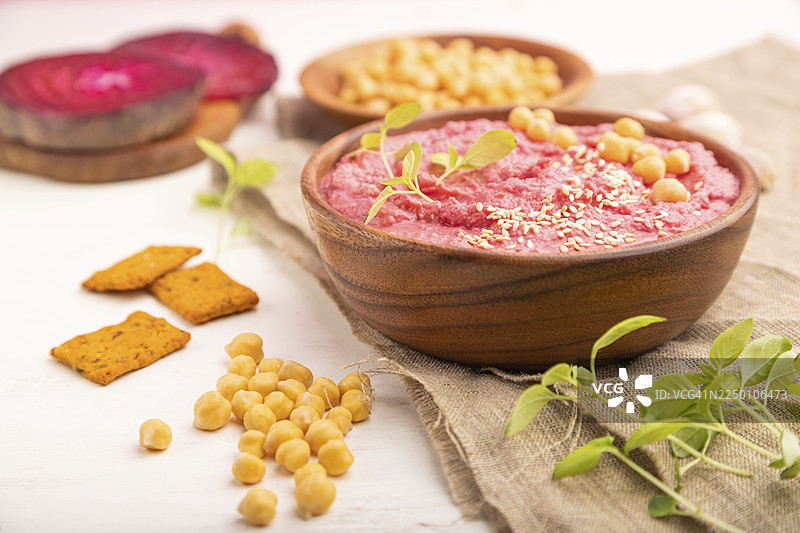 鹰嘴豆泥配甜菜和罗勒微型蔬菜苗，放在木碗中，背景为白色木材和亚麻织物。俯视，特写，选择性聚焦图片素材