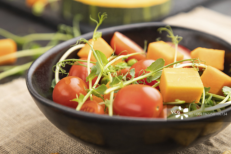 素食蔬菜沙拉，包含番茄、南瓜、微型豌豆苗，置于黑色混凝土背景和亚麻织物上。侧视，特写，选择性对焦。图片素材
