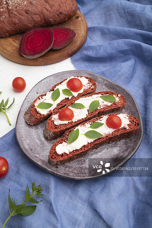 红甜菜面包三明治，配奶油芝士和番茄，放在白色混凝土背景和蓝色亚麻纺织品上。侧视图，特写。图片素材