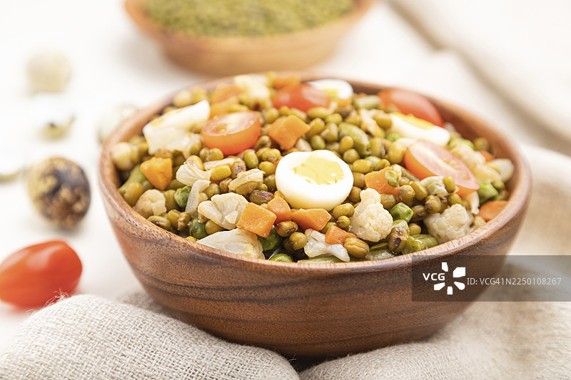 白木背景和亚麻纺织品上的绿豆粥，配以鹌鹑蛋、番茄和微型蔬菜苗。侧视图，特写，选择性对焦图片素材