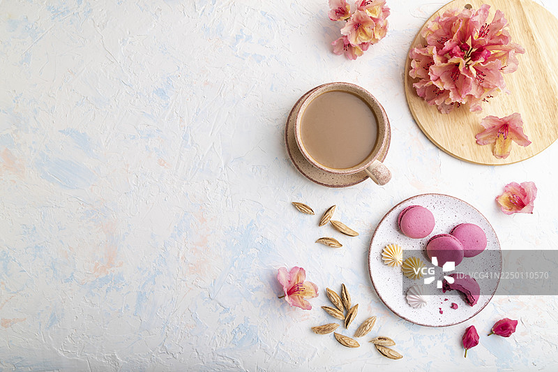 紫色马卡龙或马卡龙蛋糕配咖啡杯，背景为白色混凝土，并饰有鲜花。俯视，平铺，留白。图片素材