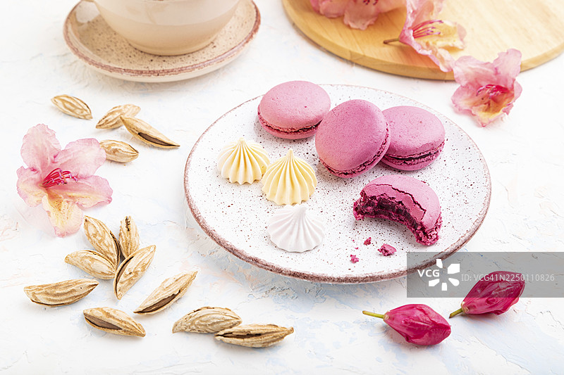 紫色的马卡龙或马卡龙蛋糕搭配一杯咖啡，背景为白色混凝土，并饰有鲜花。侧视图，特写。图片素材