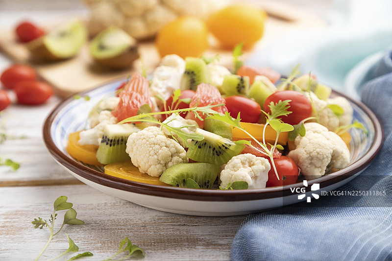 白色木质背景和蓝色亚麻布上的素食沙拉，包含菜花、卷心菜、猕猴桃、西红柿、微型蔬菜苗。侧视，特写，选择性聚焦图片素材