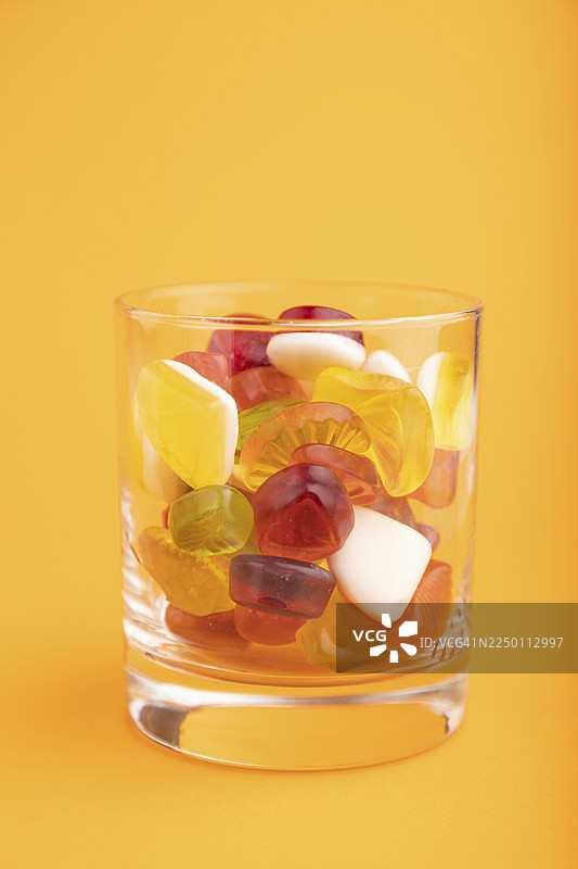 橙色柔和背景的玻璃杯中盛有各种水果果冻糖。侧视图，特写。图片素材