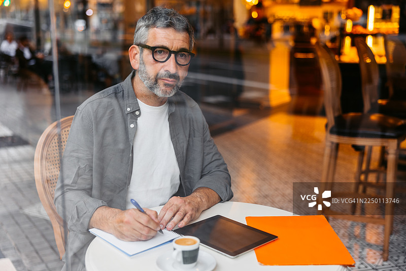 一位成熟的男士在巴塞罗那的咖啡馆里喝着咖啡，同时在一本笔记本上写字图片素材