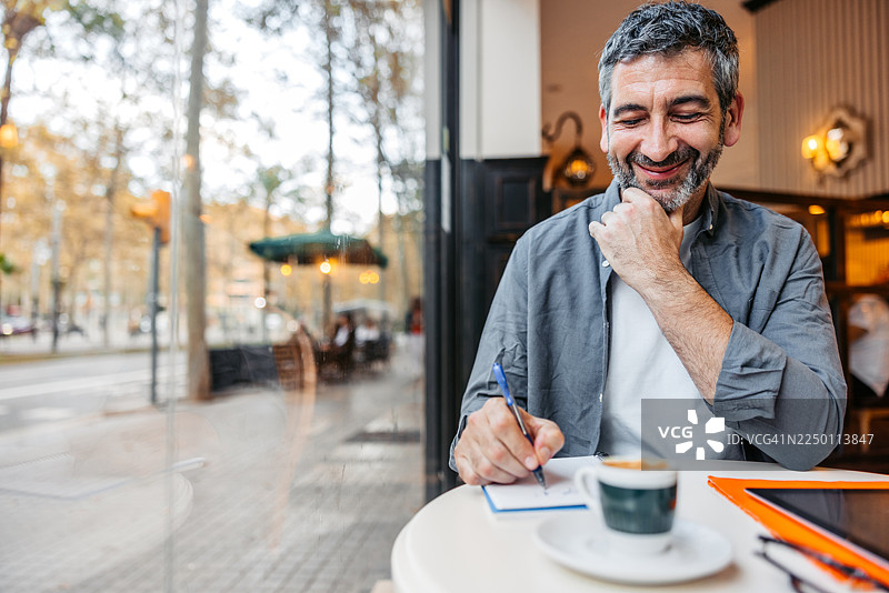 一位成熟的男士在西班牙巴塞罗那的咖啡馆里，一边喝着咖啡一边在本子上写字图片素材