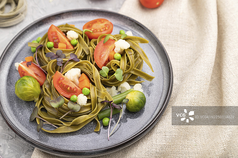 菠菜意大利面配番茄、豌豆和微型蔬菜苗，置于灰色混凝土背景和亚麻纺织品上。侧视图，特写，选择性对焦图片素材