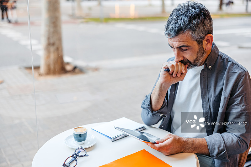 一位成熟的男士在西班牙巴塞罗那的咖啡馆里边喝咖啡边使用平板电脑图片素材
