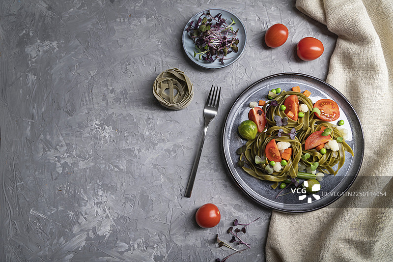 菠菜意大利宽面配番茄、豌豆和微型蔬菜苗，置于灰色混凝土背景和亚麻纺织品上。俯视、平铺、可复制空间、硬光图片素材