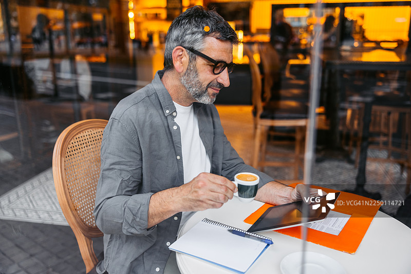 西班牙巴塞罗那咖啡馆里，一位成熟的男士一边喝咖啡一边使用平板电脑。图片素材
