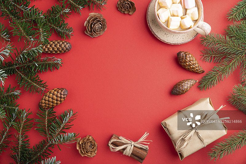 圣诞节或新年装饰画框构图。装饰品、礼盒、肉桂、松果、冷杉和云杉枝、咖啡杯，置于红色纸张背景上。俯视，留白，平面布置图。图片素材