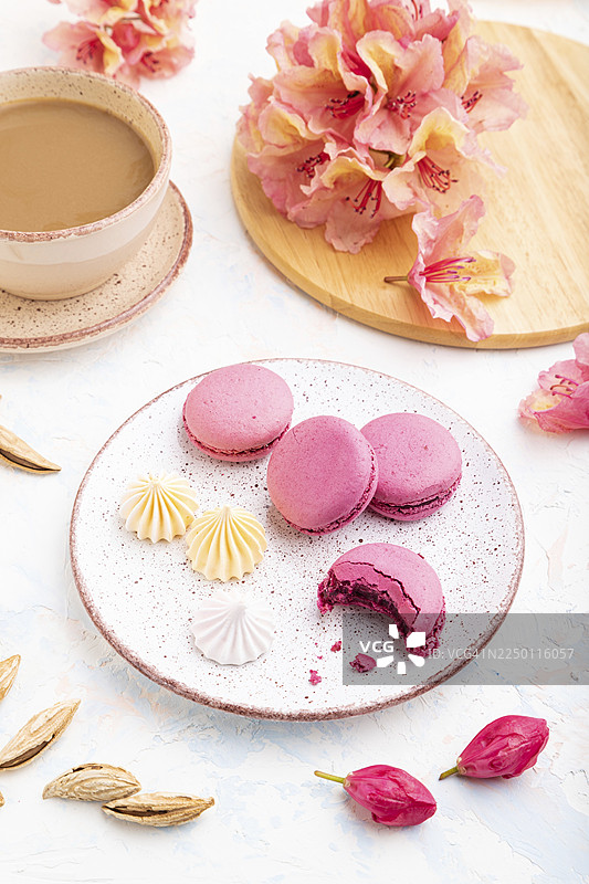 紫色的马卡龙或马卡龙蛋糕，配一杯咖啡，在带有鲜花装饰的白色混凝土背景上。侧视图，特写。图片素材