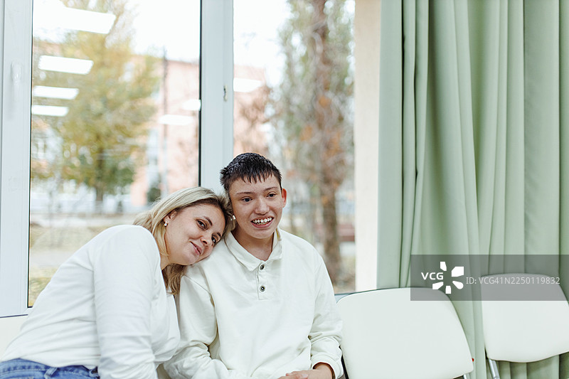 患有唐氏综合征的母亲和儿子在阳光明媚的室内温馨相拥图片素材