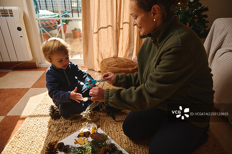 圣诞节早晨，一位母亲和孩子在家中用剪刀和松果进行手工制作。图片素材