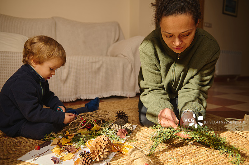 一位母亲和孩子在地毯上，用自然装饰材料进行手工制作图片素材