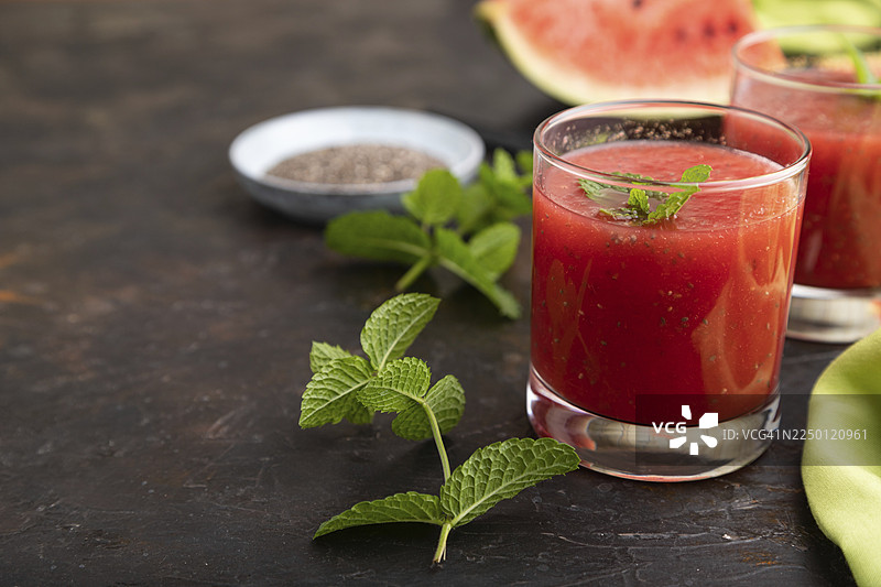 黑色混凝土背景上，带有绿色纺织品的玻璃杯中盛有西瓜汁、奇亚籽和薄荷。健康的饮品概念。侧视图，特写，选择性聚焦图片素材