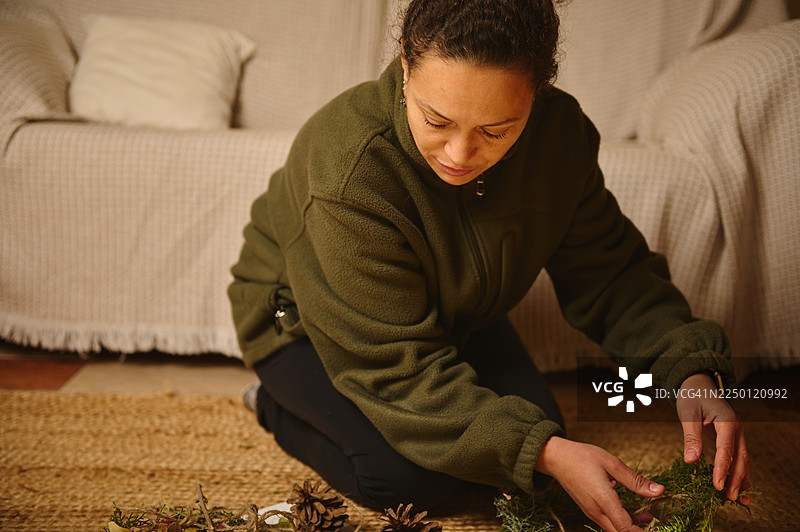 女人在地毯上布置常青枝条和松果，营造温馨的室内手工场景图片素材