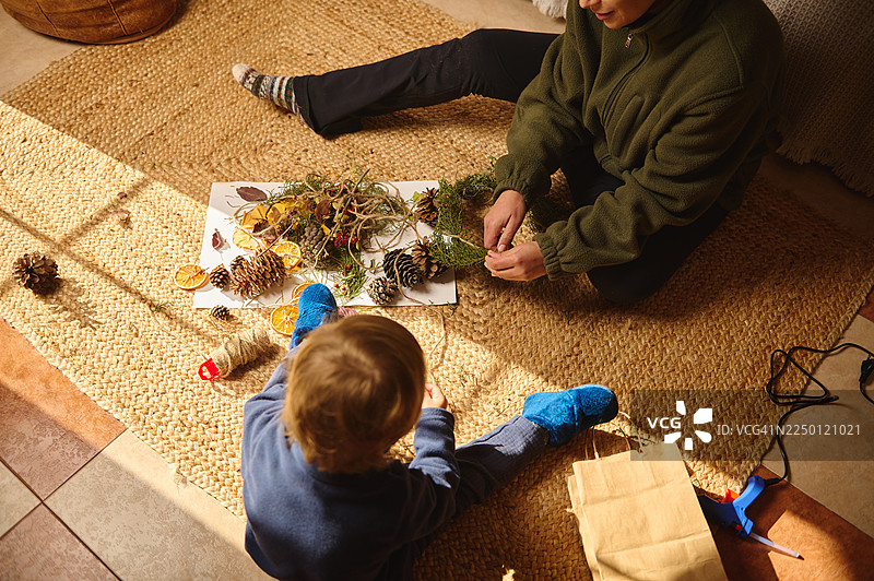 一家人在铺着松果、干橙片和绿植的地毯上进行手工制作活动图片素材