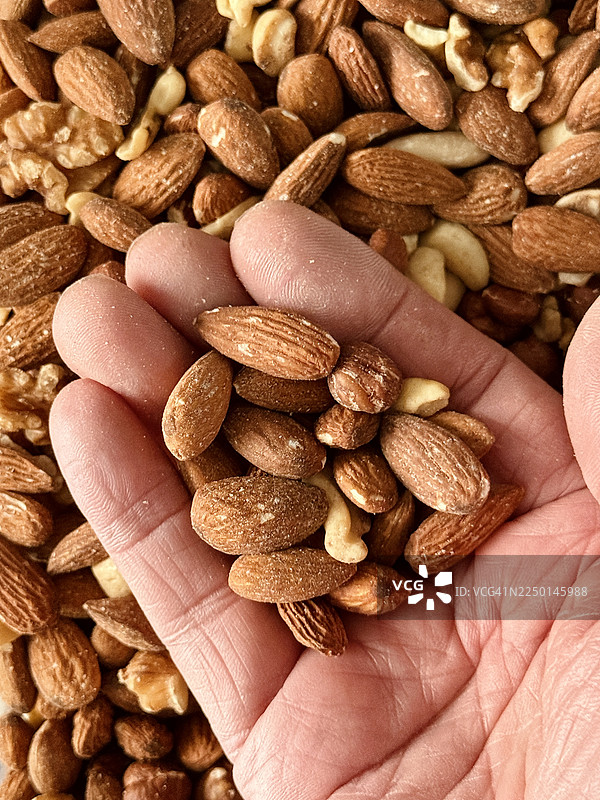 特写镜头下，一只手里抓满了包括杏仁和腰果在内的混合坚果。图片素材