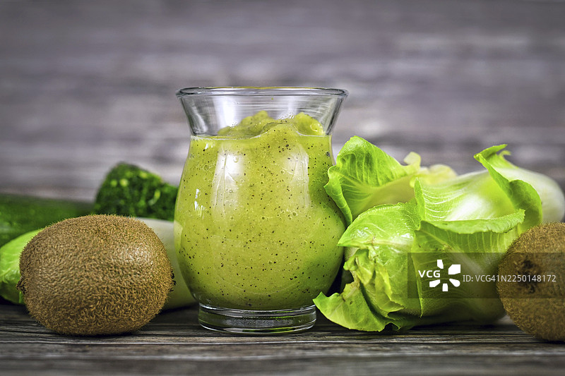 绿色蔬菜和猕猴桃围绕着盛有绿色冰沙的玻璃杯图片素材