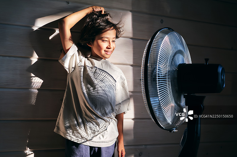 炎热的夏日，小男孩用风扇给自己扇风降温图片素材