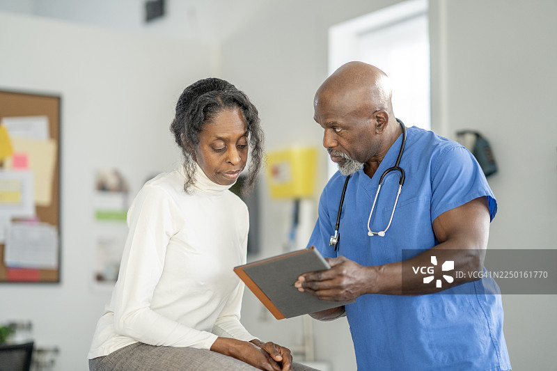 穿着蓝色手术服的黑人医生在诊所向一位老年女性解释治疗方案图片素材