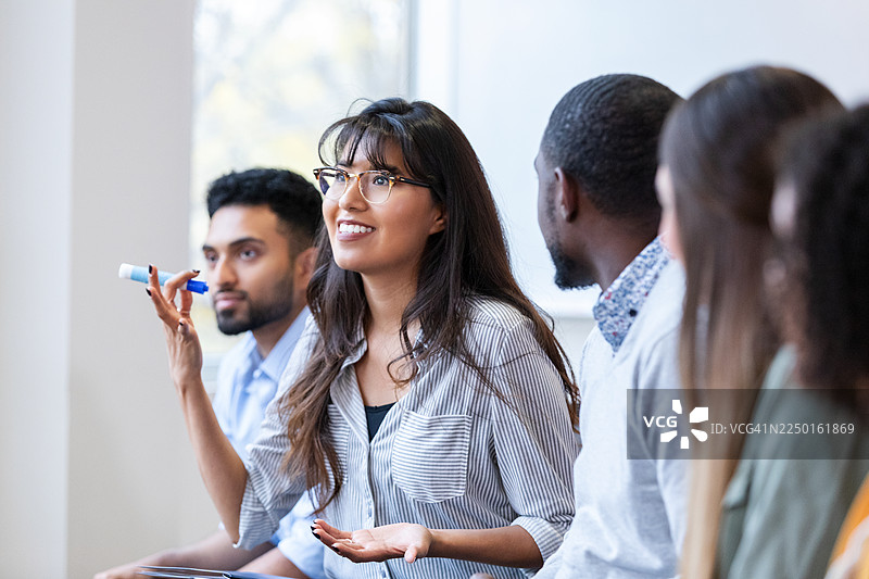 多元化团队成员在讨论，一位女士手持马克笔，一边说话一边做着手势。图片素材