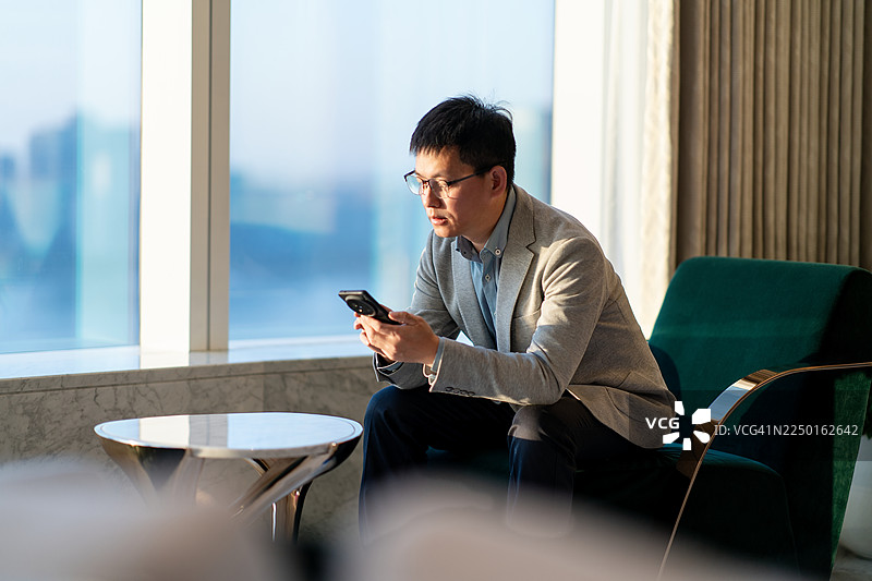 一位亚洲商人坐在椅子上使用智能手机图片素材