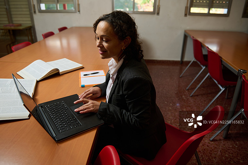 一位专业的女性在有书籍和笔记的教室里用笔记本电脑工作图片素材
