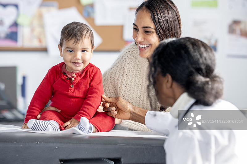 诊所里，快乐的婴儿在西班牙裔母亲和黑人医生的陪同下接受体检图片素材