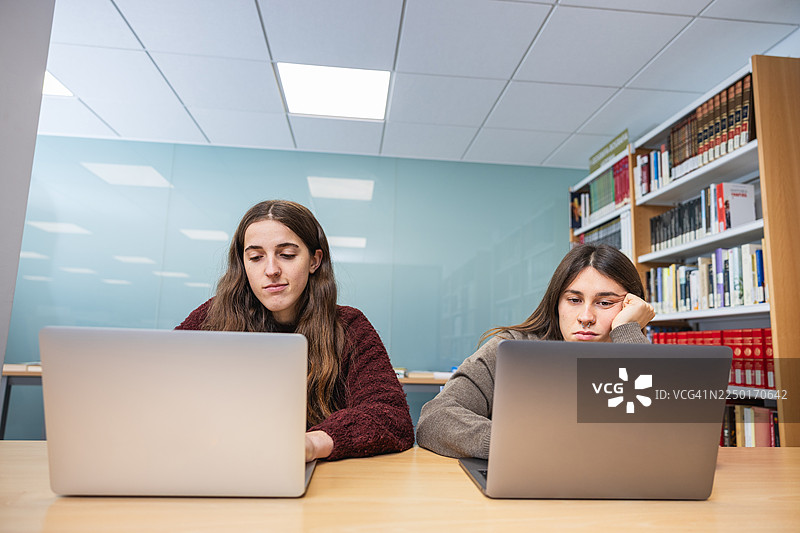 年轻的女学生在图书馆学习，感到疲惫。图片素材